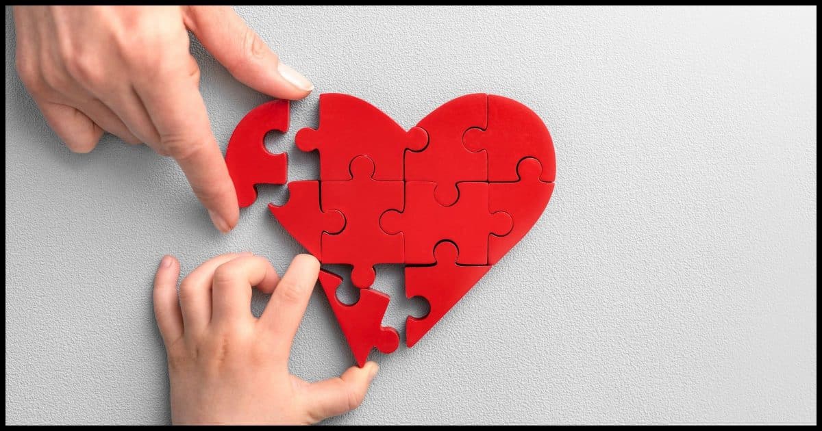 Two hands putting peices into a jigsaw puzzle heart.